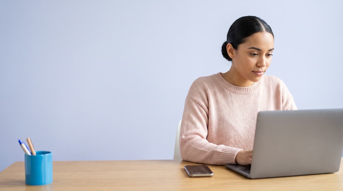 A creator at her desk edits her own short video on a laptop, her phone beside it.