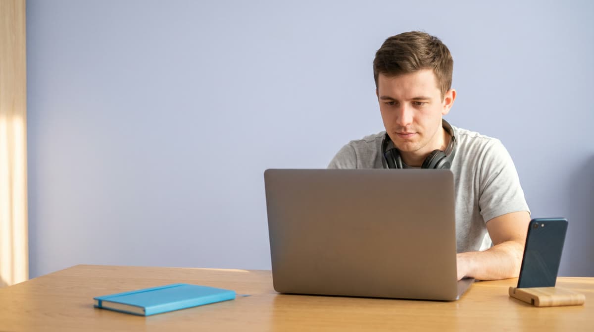 A creator at his desk edits his own short video on a laptop, his phone on a stand beside it.